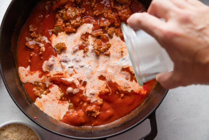 Action shot of cream being poured out of a jar and into a skillet with creamy tomato sauce.