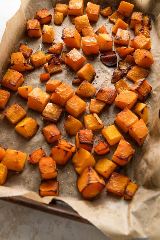Butternut squash cubes on a roasting pan just pulled out of the oven, with golden brown edges.