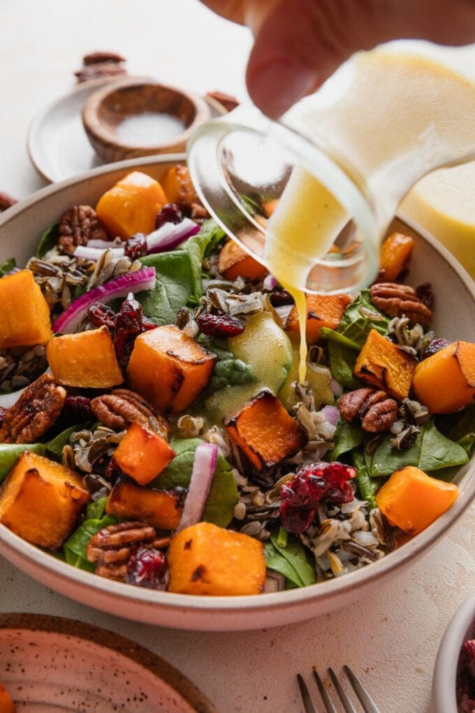 Action shot of dressing being poured on a wild rice butternut salad.
