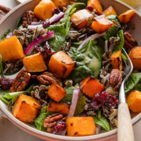 Large fork picking up a bite of wild rice salad with butternut squash and baby spinach.