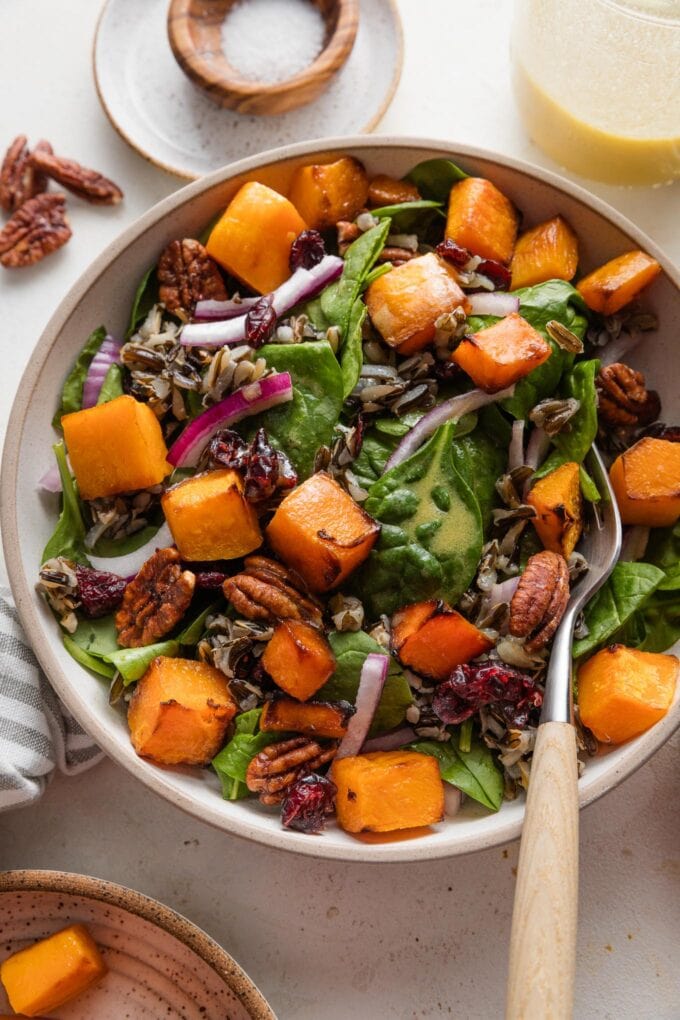 Bowl of salad with spinach, wild rice, butternut squash, dried cranberries, and pecans.