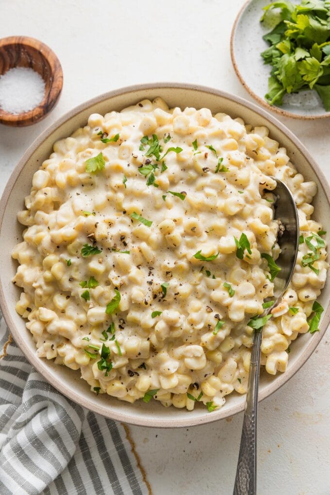 Bowl of creamed corn sprinkled with finely chopped fresh parsley.