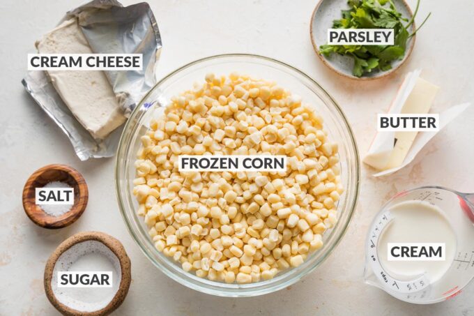 Labeled overhead photo of frozen corn kernels in a prep bowl, cream cheese, cream, butter, sugar, salt, and fresh parsley.