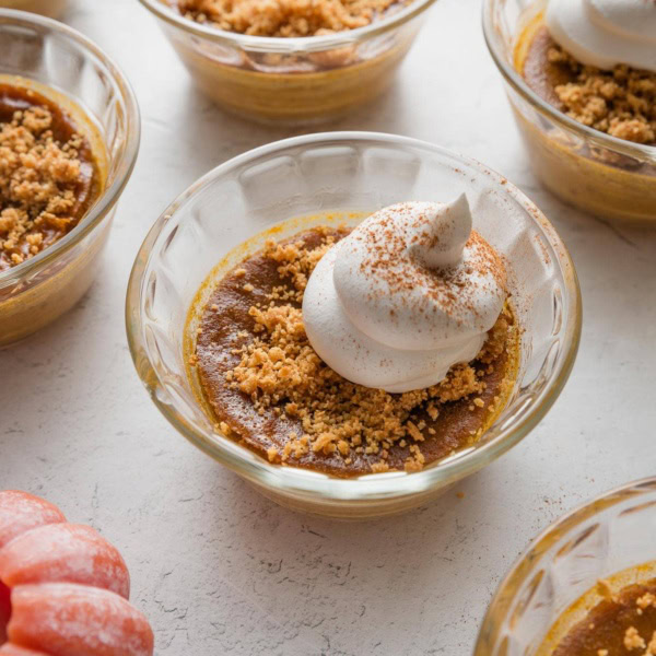 Small glass dish full of a mini pumpkin custard topped with whipped cream and graham cracker crumbs.