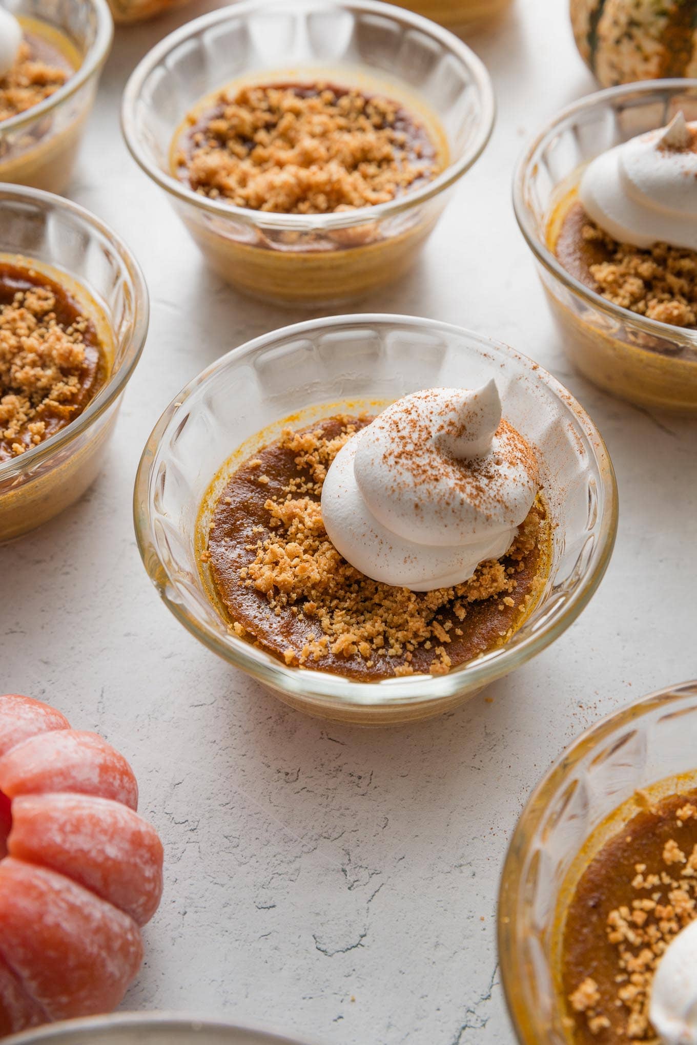 Small glass dish full of a mini pumpkin custard topped with whipped cream and graham cracker crumbs.