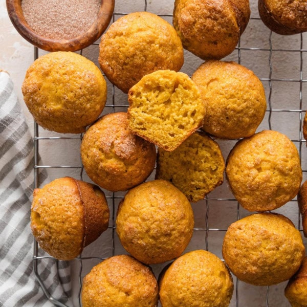 Mini pumpkin muffins cooling on a wire rack with a small bowl of cinnamon sugar topping nearby.