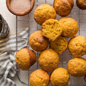 Cooling rack full of miniature pumpkin muffins with a cinnamon sugar topping.