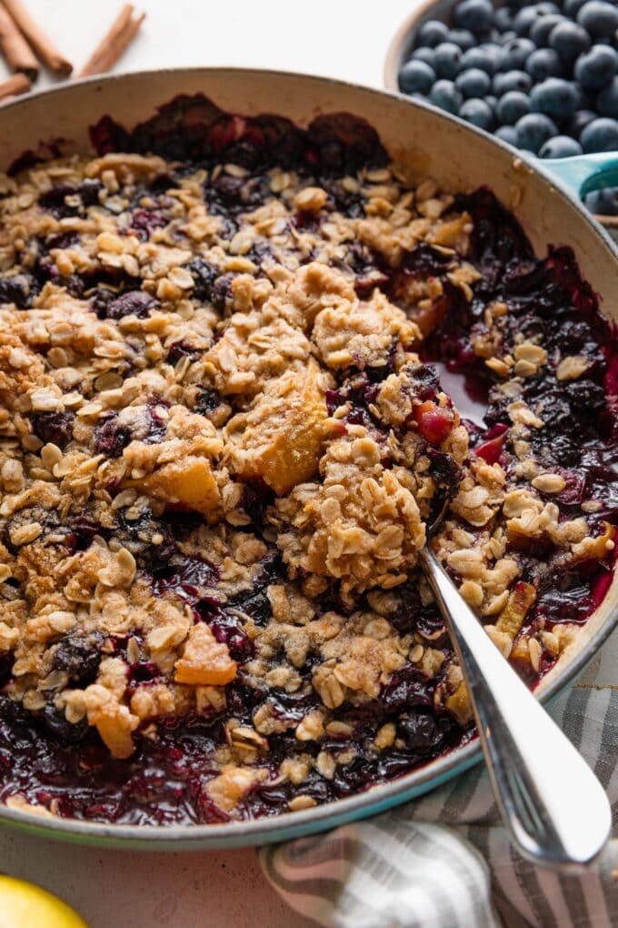 Close up of a blueberry and pear crisp with oat crumble topping served piping hot out of an oven safe skillet.