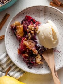 Small dish of pear blueberry crisp topped with vanilla ice cream.
