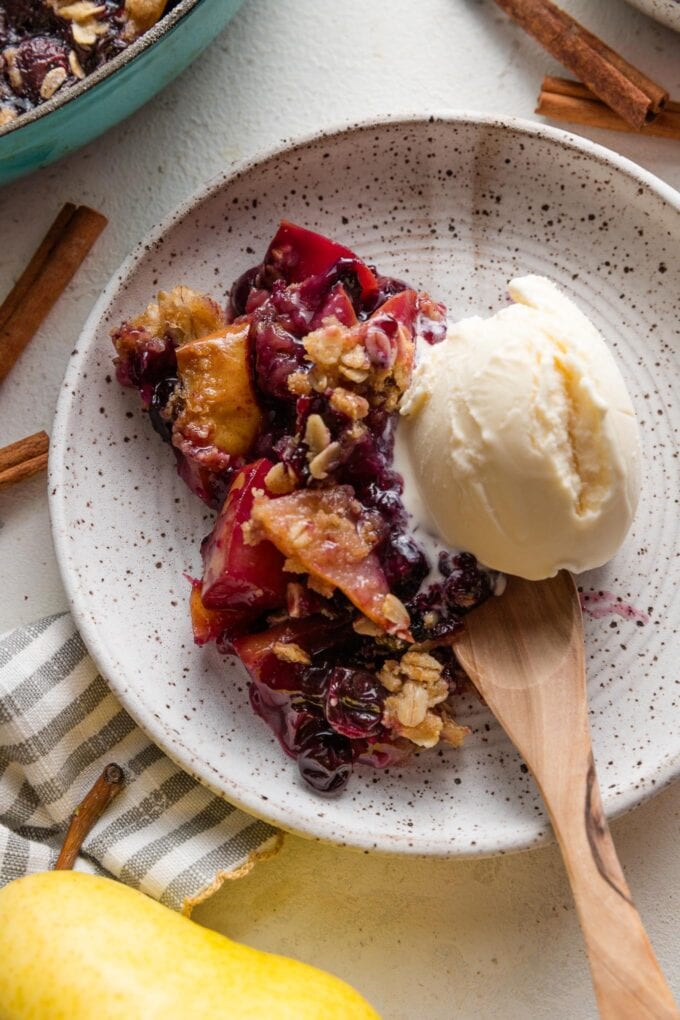 Small dish of pear blueberry crisp topped with vanilla ice cream.