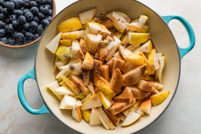 Chopped pears simmering in a skillet with maple syrup, vanilla, and spices.