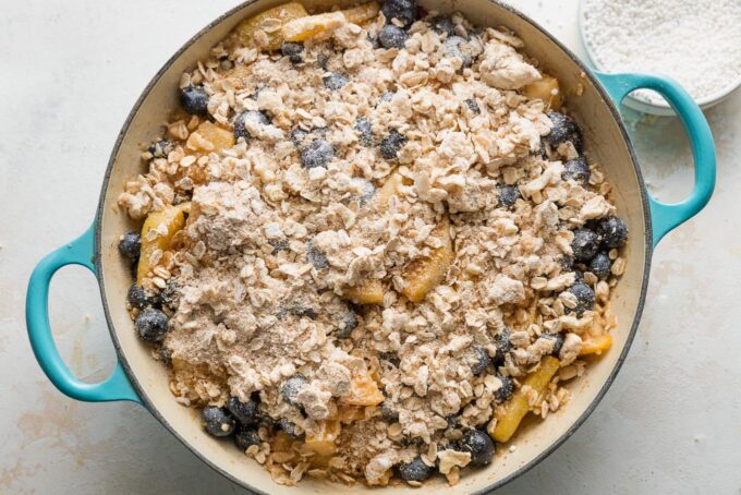 Buttery oat topping spread on top of a blueberry pear fruit dessert filling.