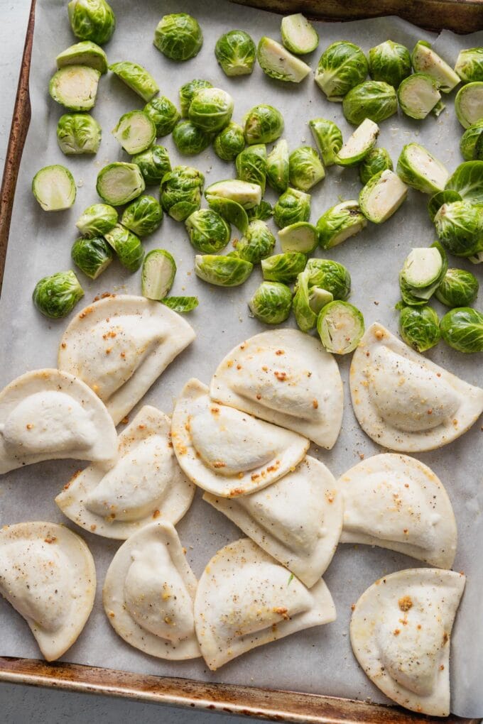 Uncooked Brussels sprouts and pierogies spread out on a rimmed sheet pan lined with parchment.