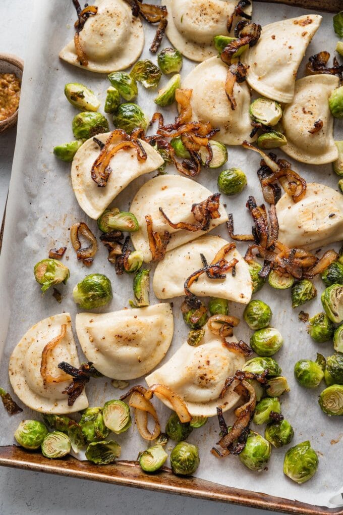 Large rimmed sheet pan with roasted pierogies, Brussels sprouts, and caramelized onions.
