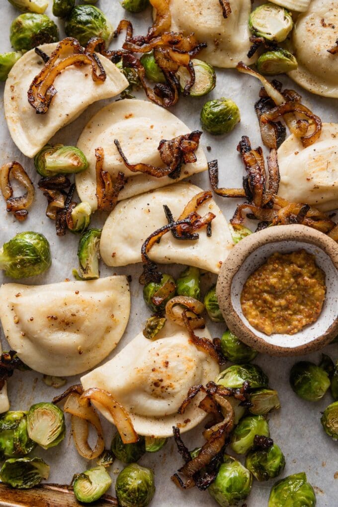 Close up of pierogies and Brussels sprouts on a sheet pan and topped with caramelized onions.