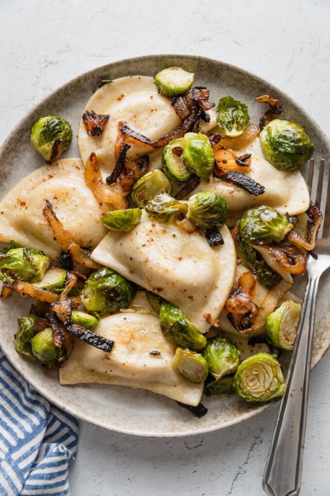 Small plate filled with a simple meal of pierogies, roasted Brussels sprouts, and caramelized onions.