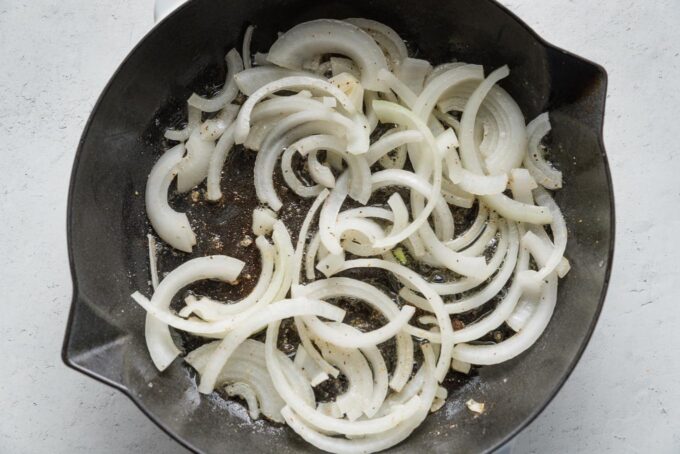 Thinly-sliced onion sizzling in a cast iron pan with butter.