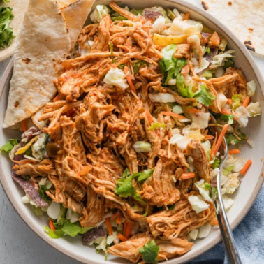 Instant Pot shredded Mexican chicken with salsa served over a Southwestern style salad kit with a tortilla on the side.