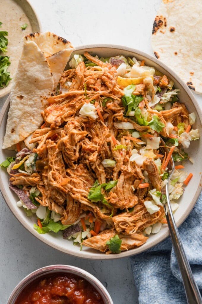 Instant Pot shredded Mexican chicken with salsa served over a Southwestern style salad kit with a tortilla on the side.