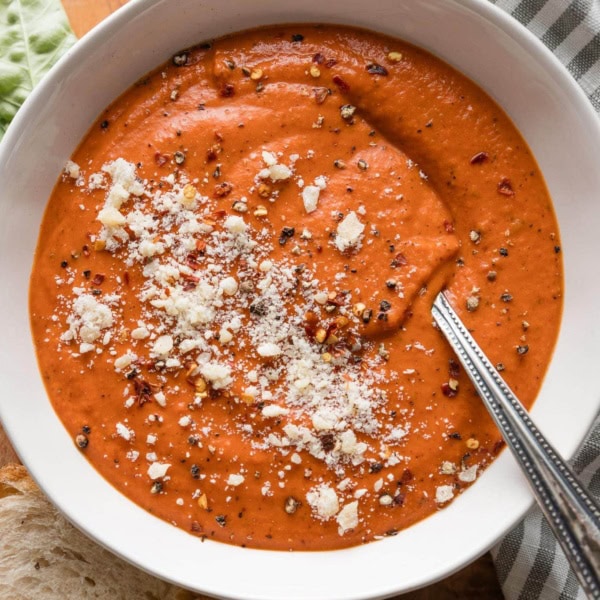Bowl of tomato bisque with butternut squash garnished with a generous sprinkle of Parmesan cheese and fresh-cracked black pepper.