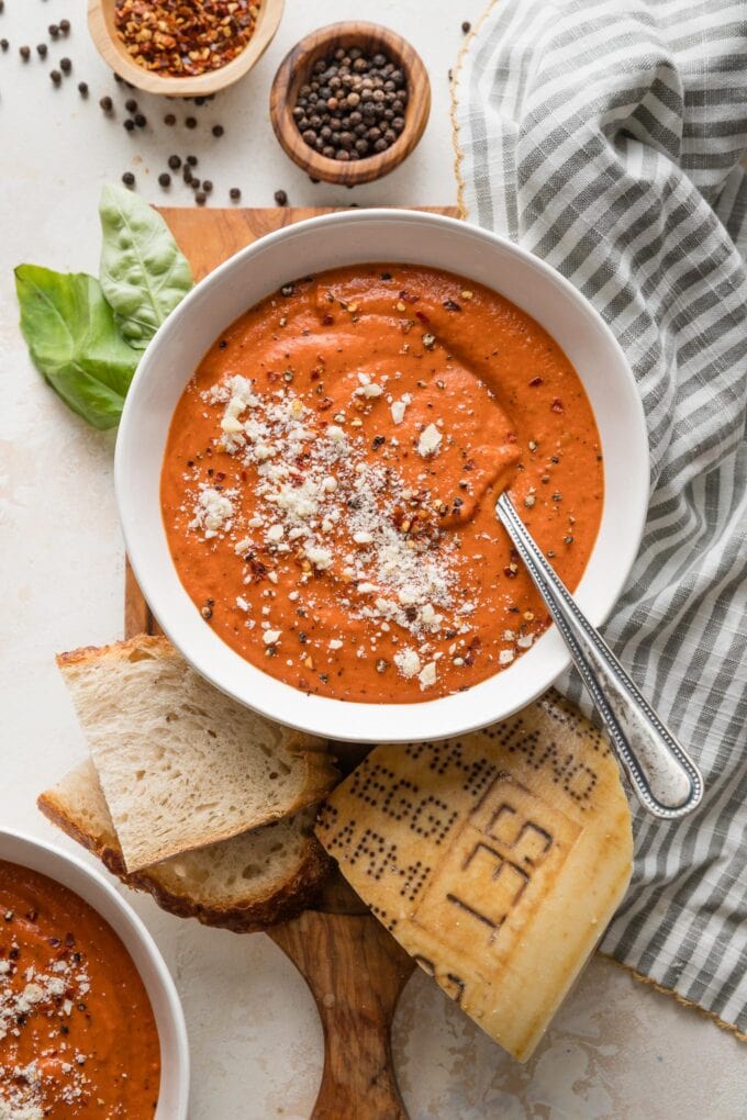 Countertop set with bowls of tomato butternut bisque, sliced sourdough bread, and garnishes of herbs and fresh Parmesan.