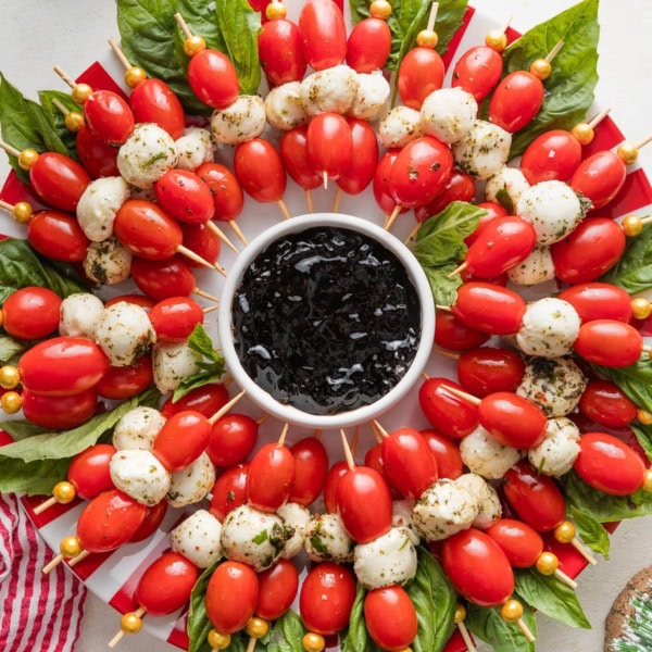 Caprese skewers arranged to look like a wreath with a small bowl of balsamic glaze in the middle.