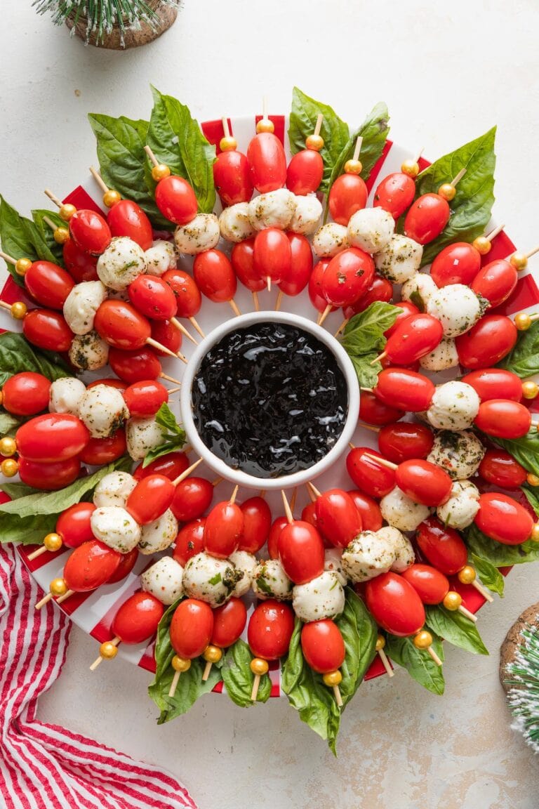 Caprese skewers arranged to look like a wreath with a small bowl of balsamic glaze in the middle.