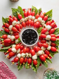 Caprese skewers arranged to look like a wreath with a small bowl of balsamic glaze in the middle.