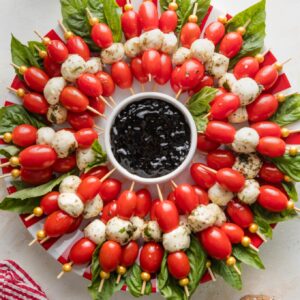 Caprese skewers arranged to look like a wreath with a small bowl of balsamic glaze in the middle.