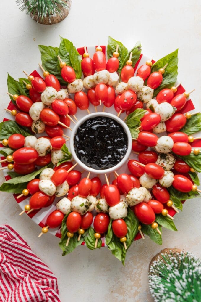 Caprese skewers arranged to look like a wreath with a small bowl of balsamic glaze in the middle.