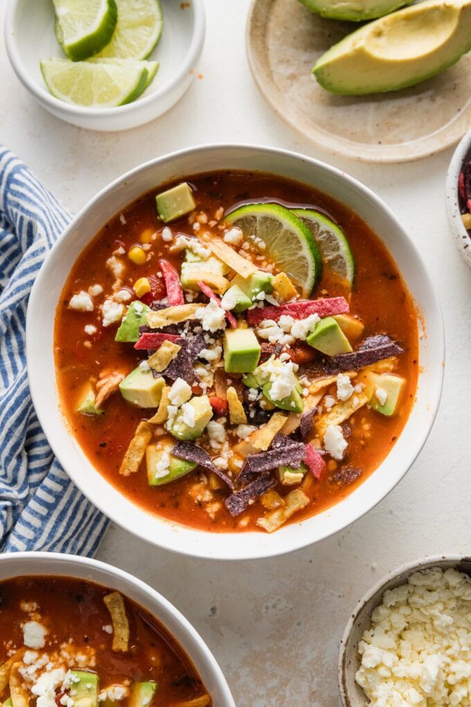 Bowl of chipotle chicken tortilla soup on a counter with extra avocado and Cotija nearby.