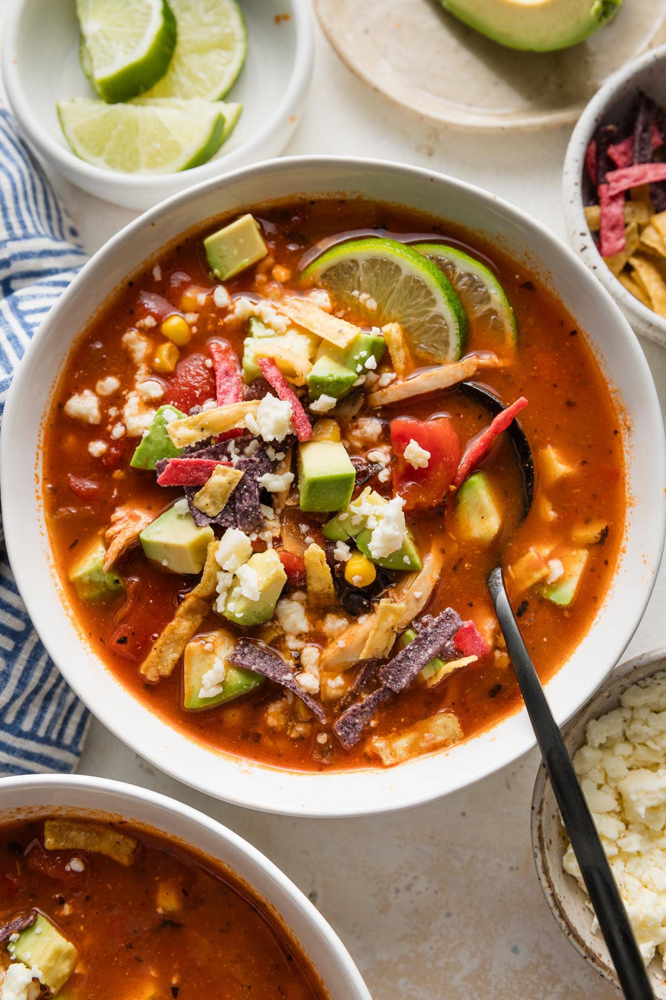 Overhead view of a bowl of chicken chipotle tortilla soup topped with tortilla strips, avocado, and lime wedges.