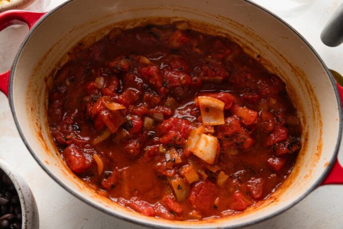 Diced tomatoes stirred into an oval Dutch oven.