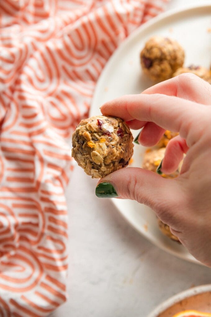 Close up of a woman's hand holding a cranberry orange protein bite over a patterned orange napkin.