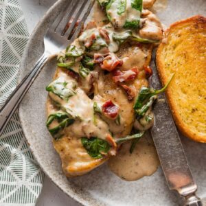 Plate with a chicken breast served in a balsamic cream sauce with crisp bacon bits and wilted baby spinach.