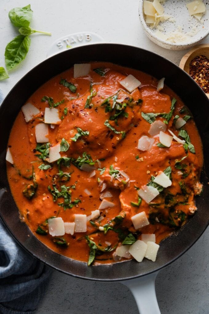 Overhead view of a cast iron skillet filled with creamy tomato sauce and chicken breasts.