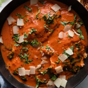 Cast iron skillet resting on the kitchen counter, filled with a creamy tomato chicken dish with basil and Parmesan.