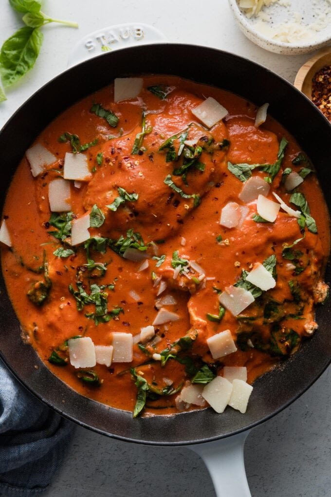 Cast iron skillet resting on the kitchen counter, filled with a creamy tomato chicken dish with basil and Parmesan.