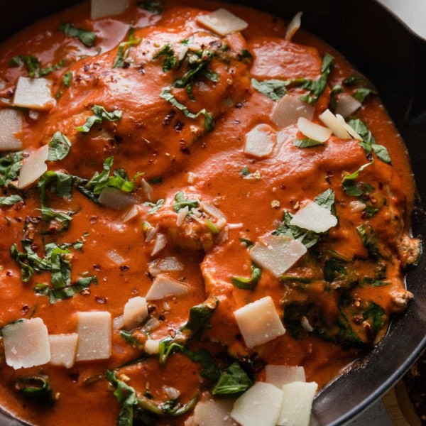 Close up of a chicken breast simmered in a creamy homemade tomato sauce with fresh spinach, basil, and Parmesan.