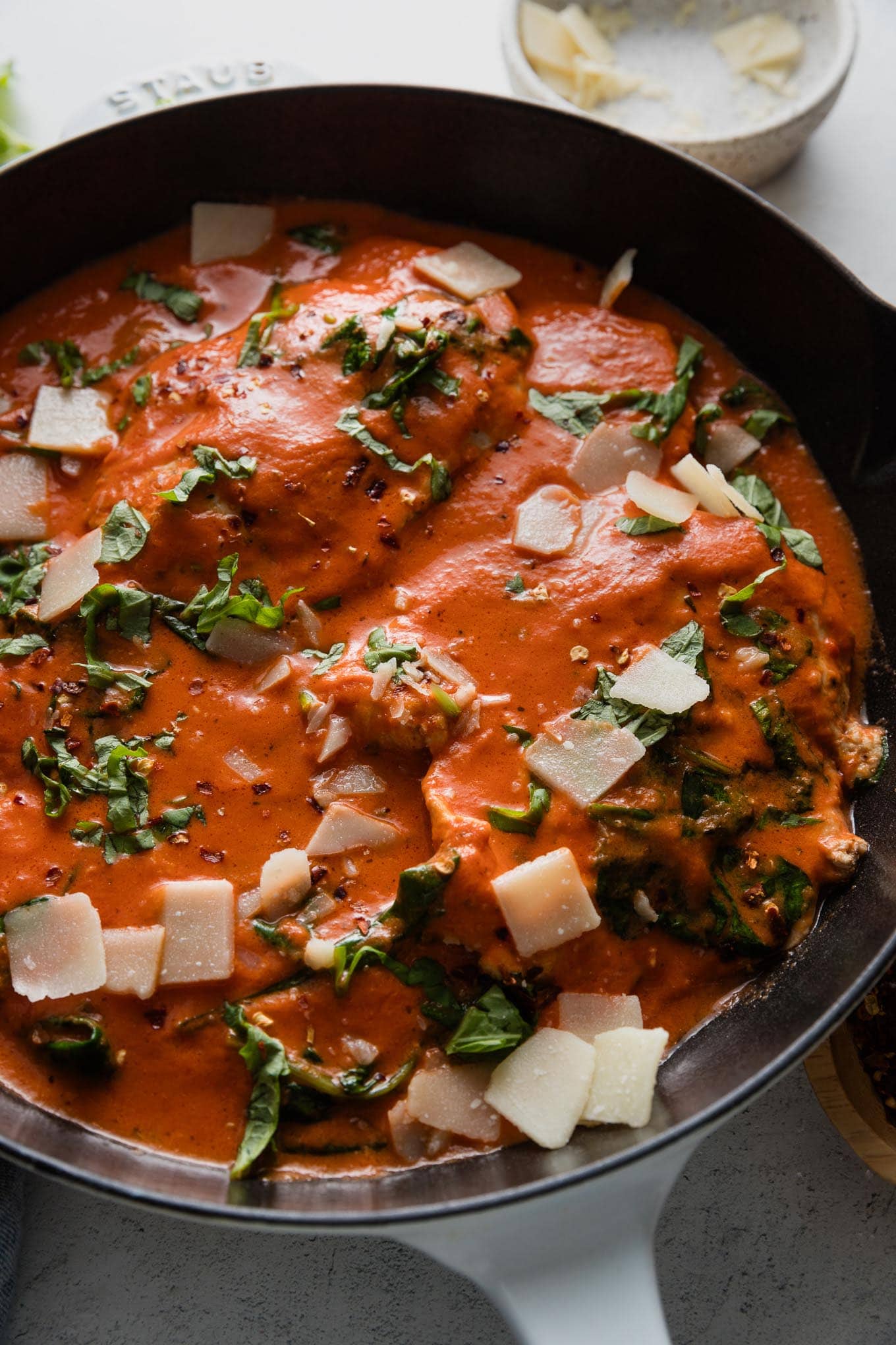 Close up of a chicken breast simmered in a creamy homemade tomato sauce with fresh spinach, basil, and Parmesan.