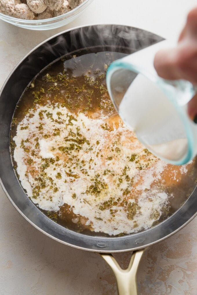 Cream being poured into a simmering beef-based sauce in a skillet.