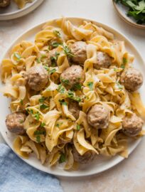 Plate full of Swedish meatballs with egg noodles and fresh parsley.