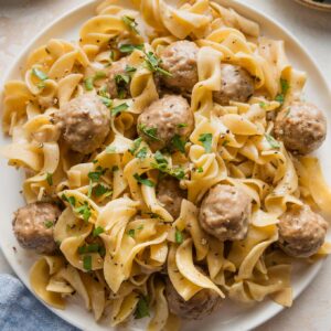 Plate full of Swedish meatballs with egg noodles and fresh parsley.