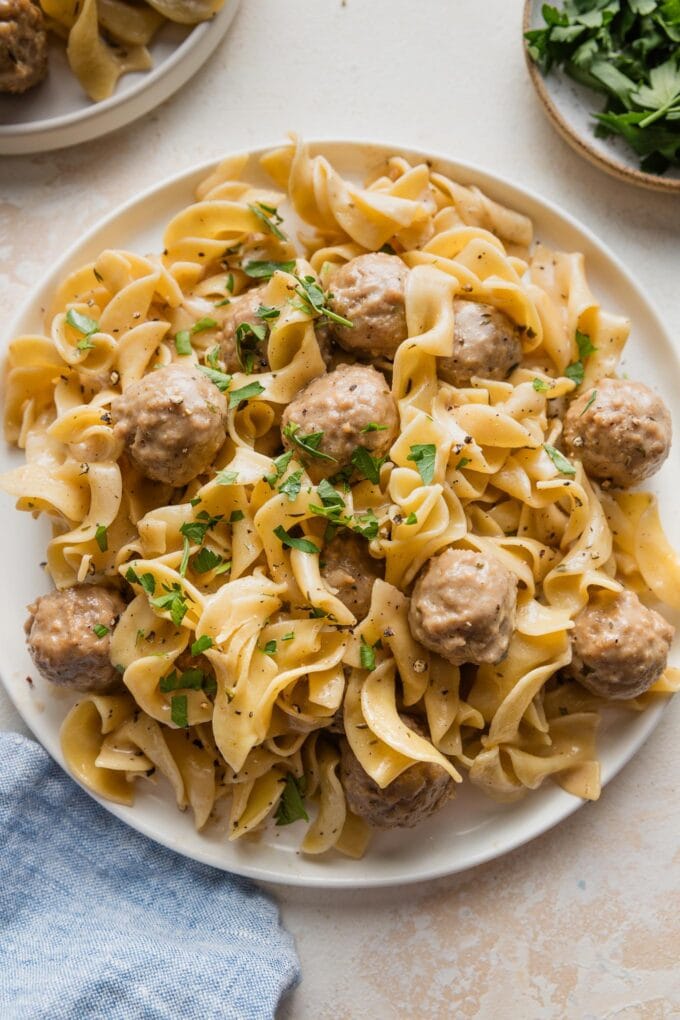 Plate full of Swedish meatballs with egg noodles and fresh parsley.