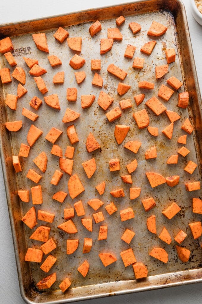 Sheet pan full of diced sweet potatoes seasoned with chili powder and cumin.