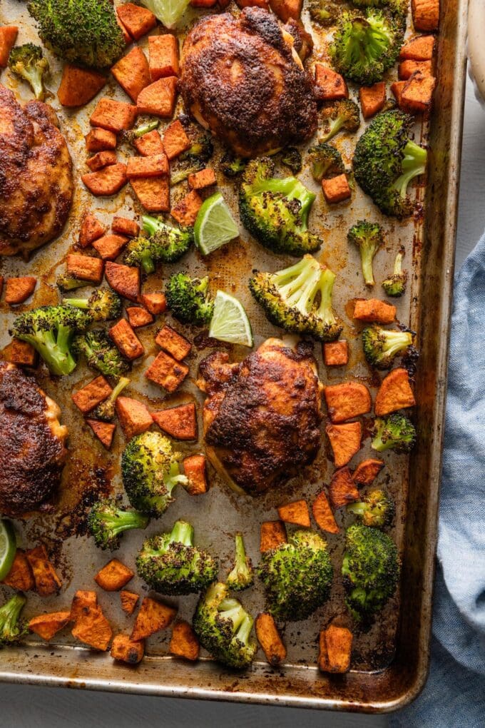 Large rimmed sheet pan full of chipotle chicken thighs, diced sweet potatoes, and broccoli.