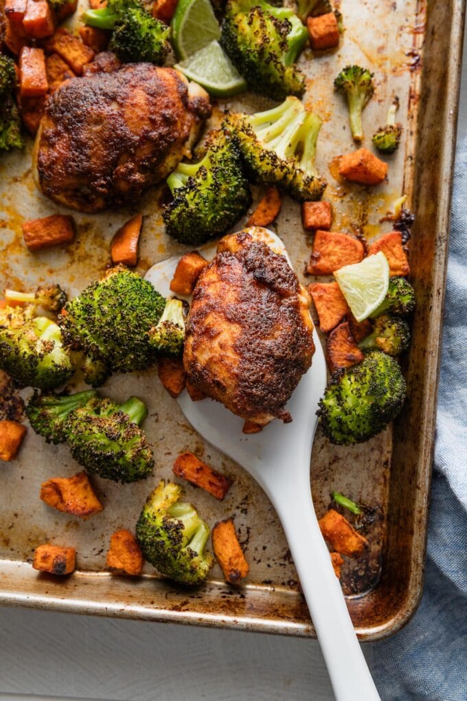Spatula lifting a chipotle-seasoned chicken thigh off of a sheet pan.