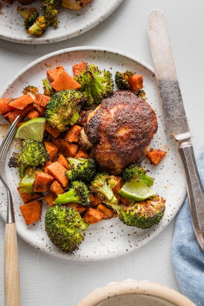 Plate with a chicken thigh roasted and seasoned with a chipotle spice rub, roasted sweet potatoes with a chili-cumin seasoning, and broccoli florets.