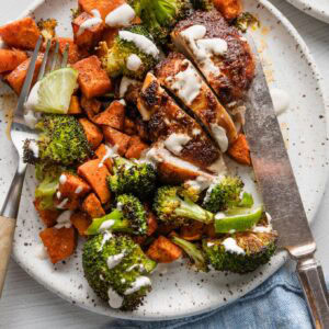 Sheet pan chipotle chicken thighs served with sweet potato, broccoli, and a simple lime crema.