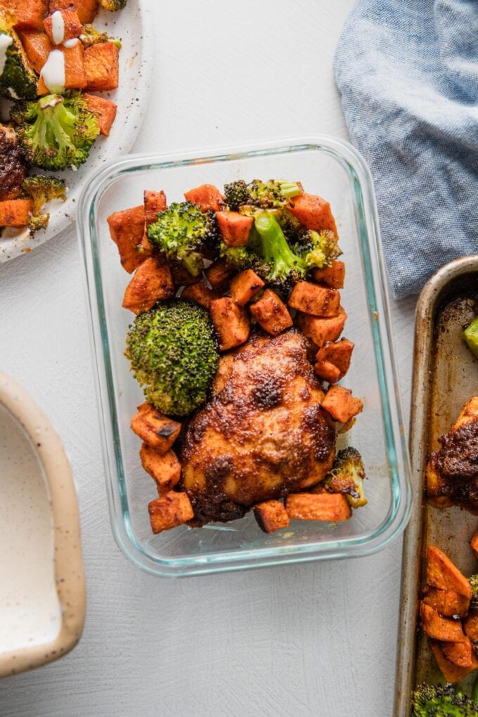 Glass meal prep container with a portion of chipotle-seasoned chicken thighs, sweet potatoes, and broccoli.